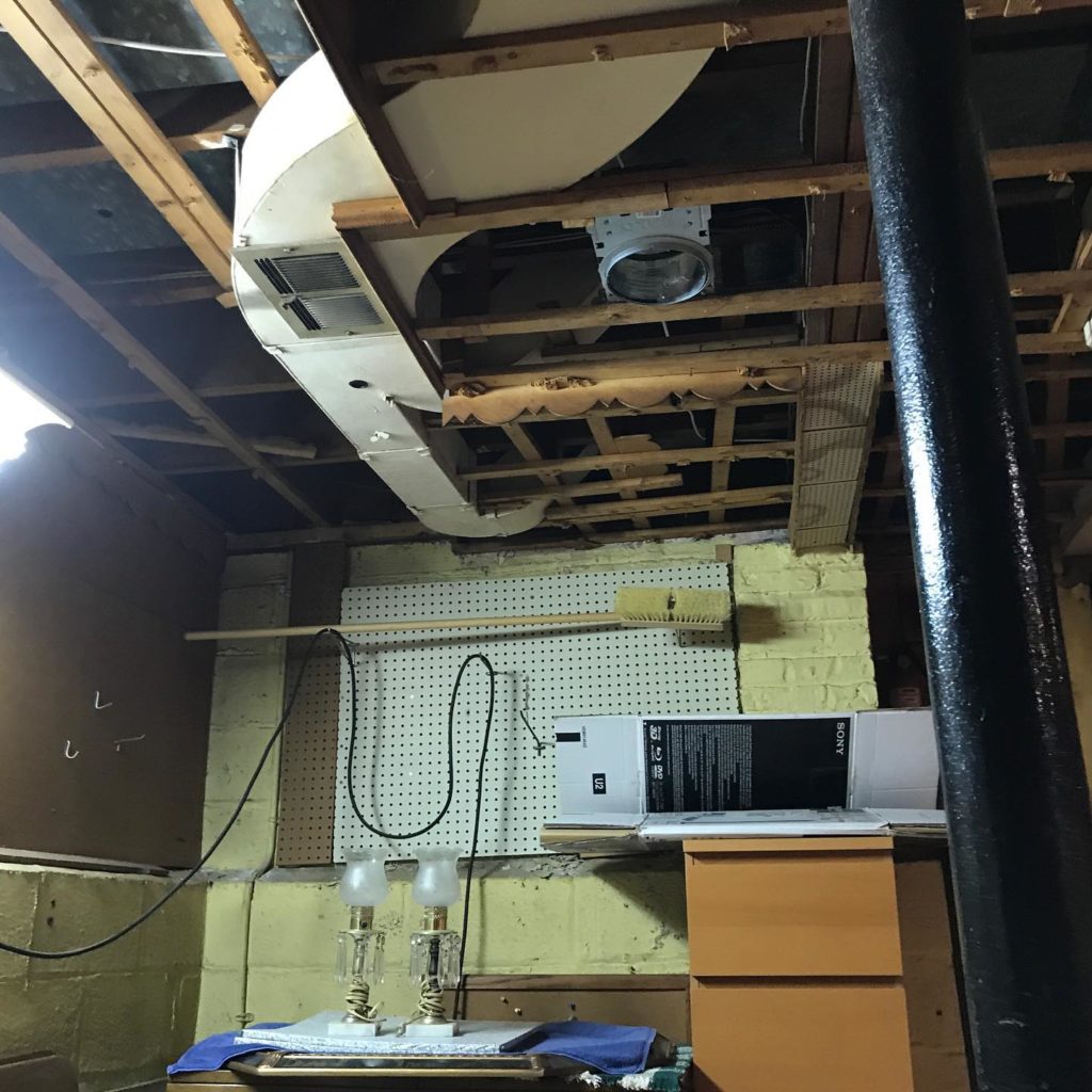 Basement with exposed ceiling, ductwork, pegboard wall, and some stored items.