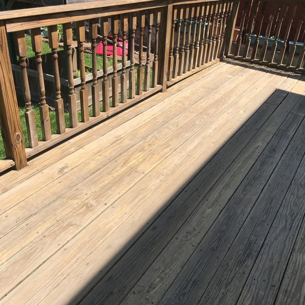 Sunlit wooden deck with railing, showing clean and weathered boards.