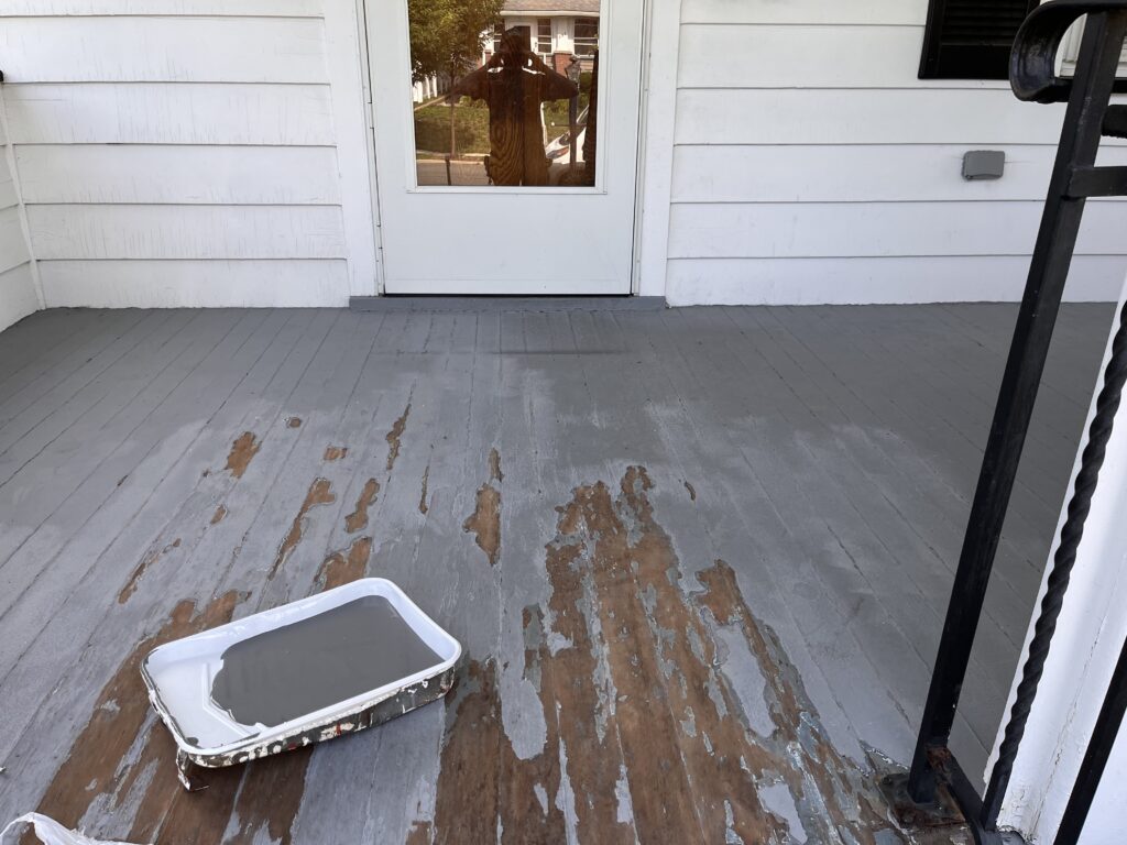 Partially painted front porch with peeling old paint and a tray of gray paint in progress.